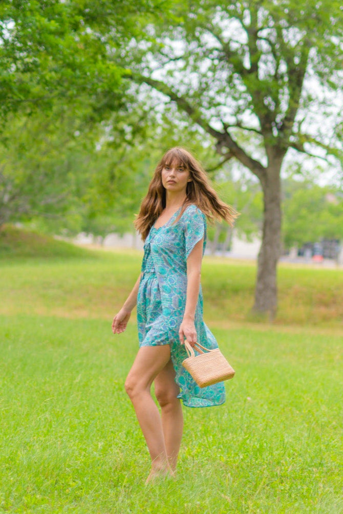 Woman in a blue dress standing in a grassy park with trees in the background