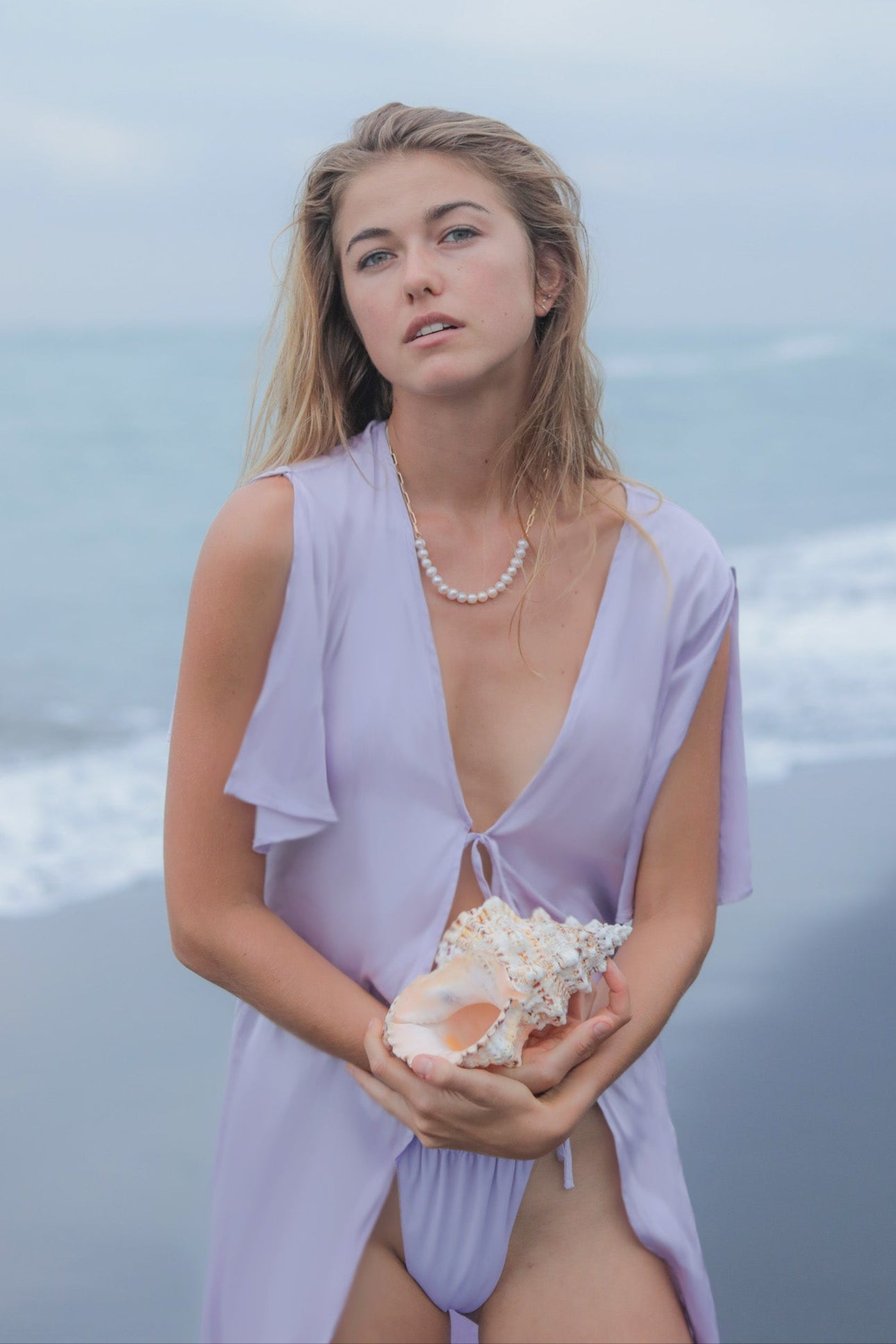 Woman in a purple cover-up holding a shell on a beach